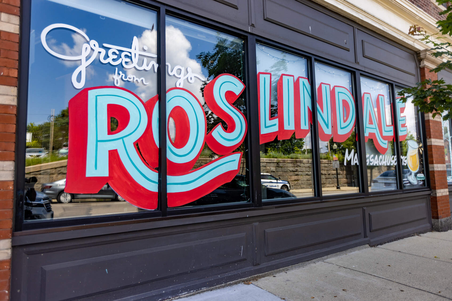 "Greetings from Roslindale, Massachusetts" is painted on the storefront of Distraction Brewing in Roslindale. (Jesse Costa/WBUR)