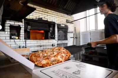 A worker at Frank Pepe Pizzeria Napoletana takes a piping hot pizza out of a coal oven and places it into a to-go box during a weekday lunchtime rush. The restaurant was founded in 1925 by Italian immigrant Frank Pepe in New Haven, and has since opened locations across the Northeast.